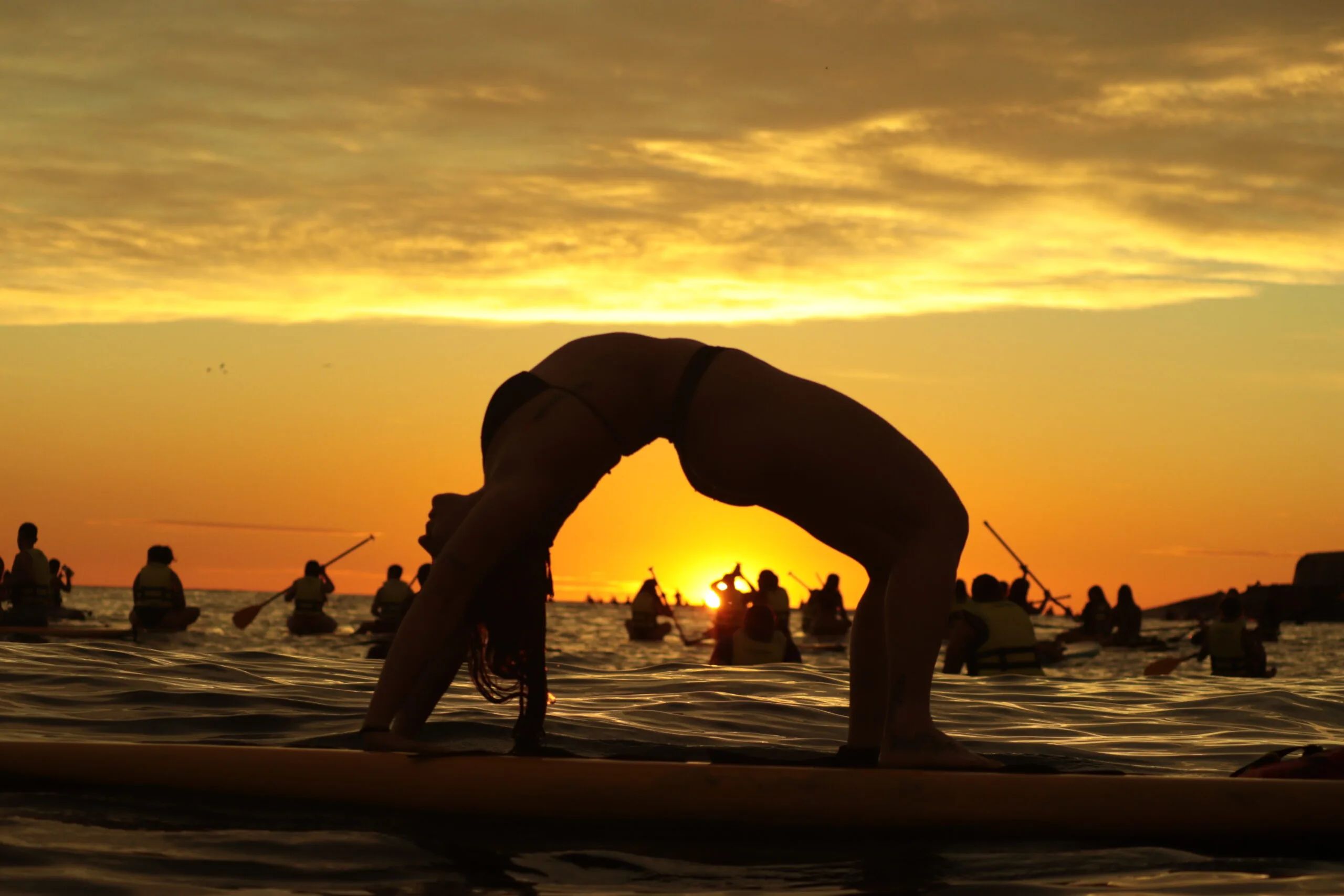 Mulher fazendo ponte sobre prancha no mar durante stand up paddle Copacabana ao pôr do sol, silhueta destacada, experiência nascer do sol copacabana.
